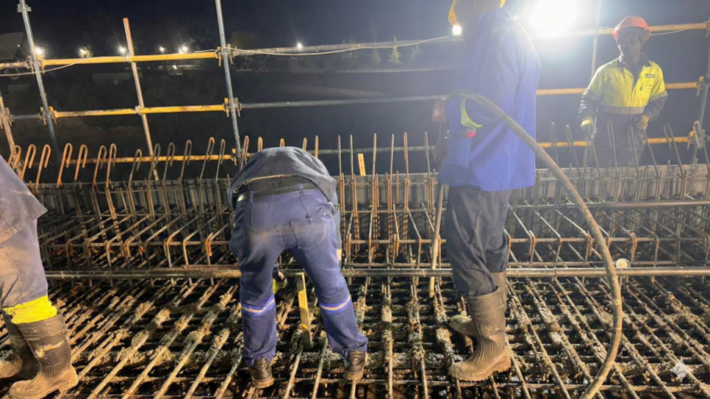 Injumo Development construction team working a night shift, pouring concrete into a heavy steel reinforcement grid under floodlights.